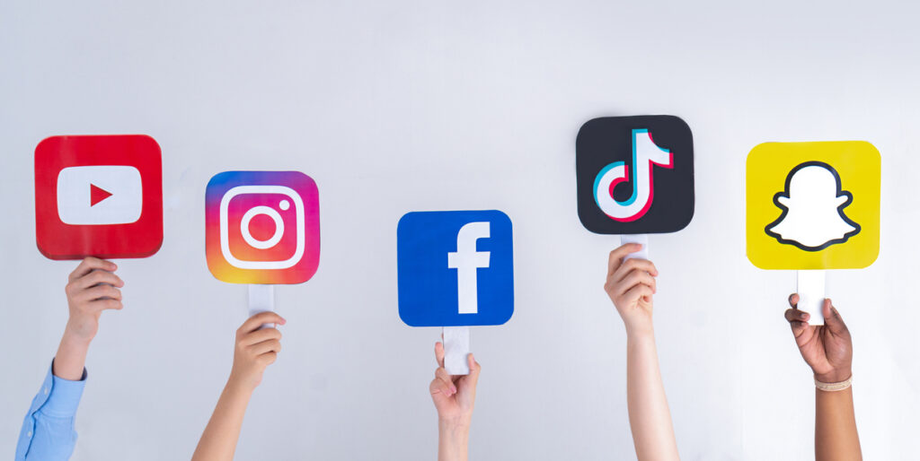 hands holding up signs with logos of social media platforms - youtube, instagram, facebook, ticktok, snapchat